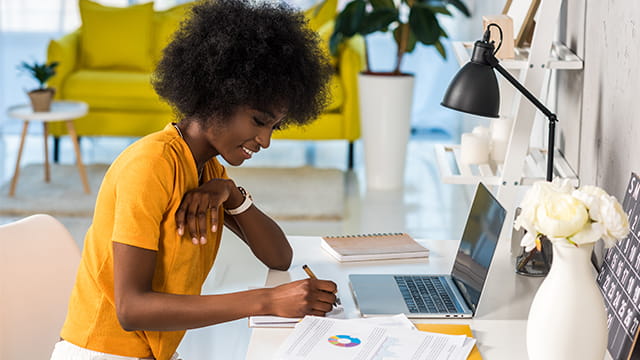 Woman sitting at a desk writing with a laptop. 